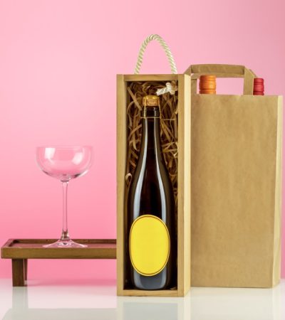 Eco friendly wine shop, bar winery or wine delivery concept. Mockup of bottle of champaign in a wooden box with wine glass and bottles of wine in paper bag on pink background. Ecologic packaging